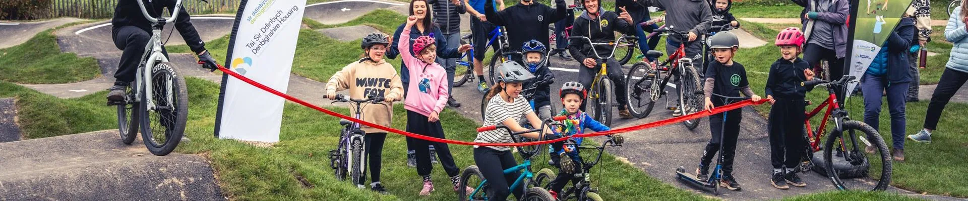 Grŵp o blant ac oedolion yn dathlu y tu ôl i raff goch ar gyfer Prosiect Egnïol Sir Ddinbych.