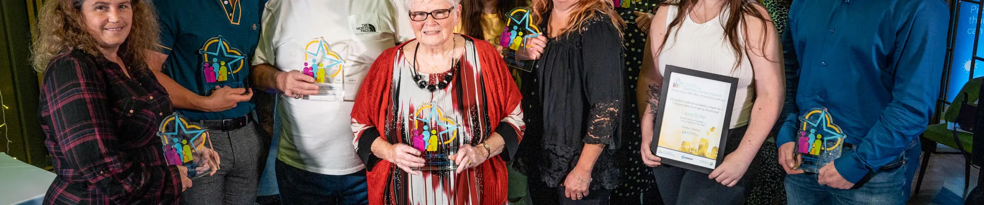 Grŵp o bobl yn gwenu ac yn dal gwobrau gwydr yng ngwobrau Tai a Thenantiaeth Sir Ddinbych.