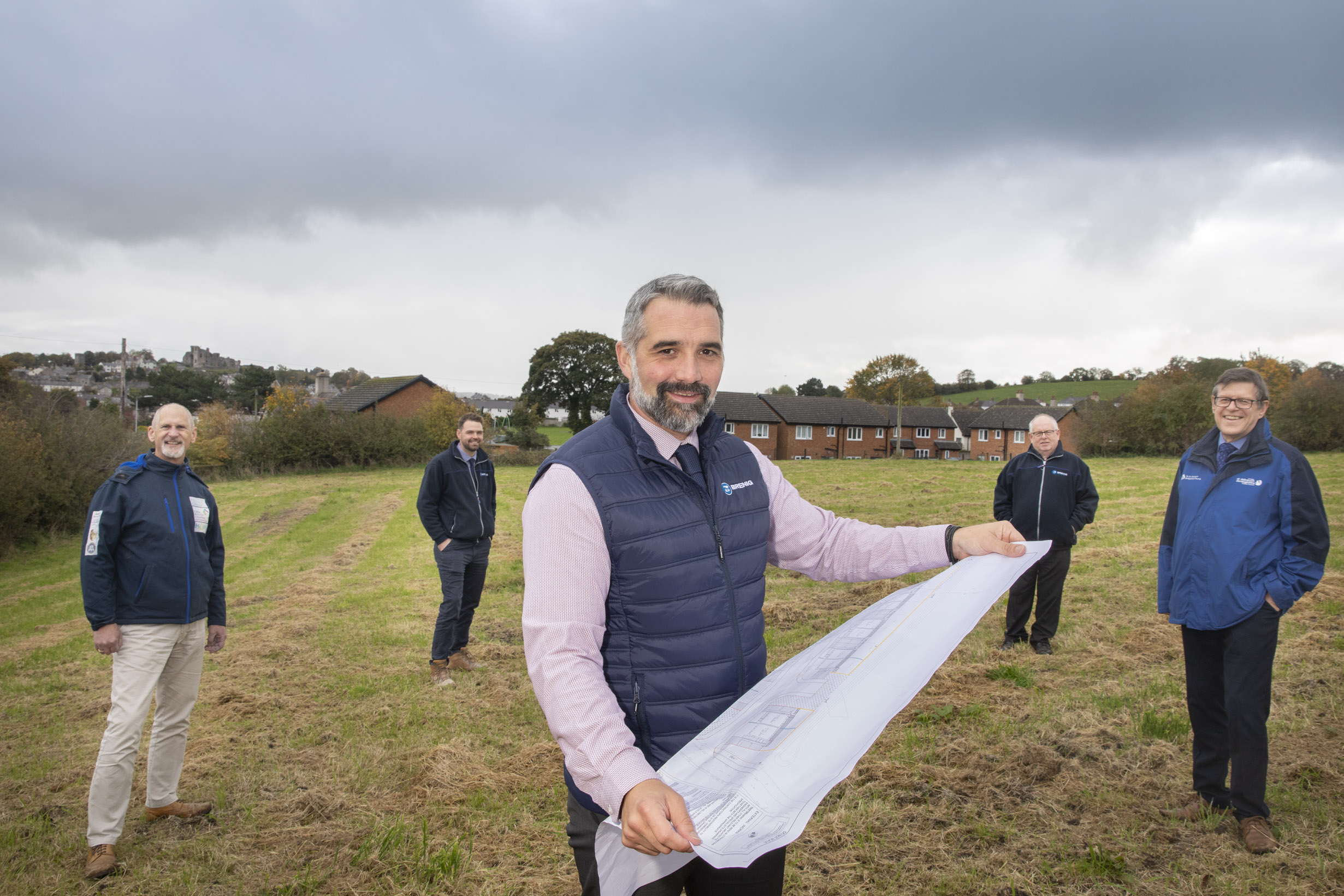 Five men stand together on an area of open land with a housing development plan
