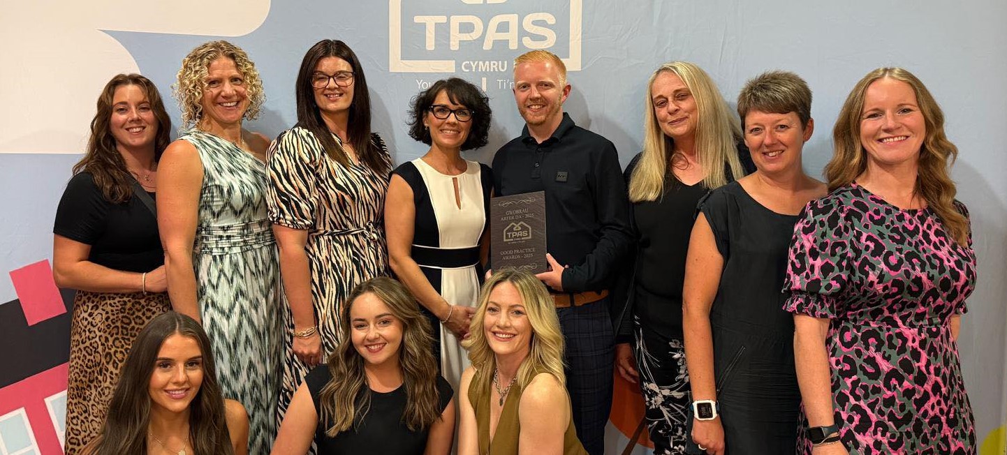A group of people stand together with the TPAS Cymru Good Practice Award plaque.