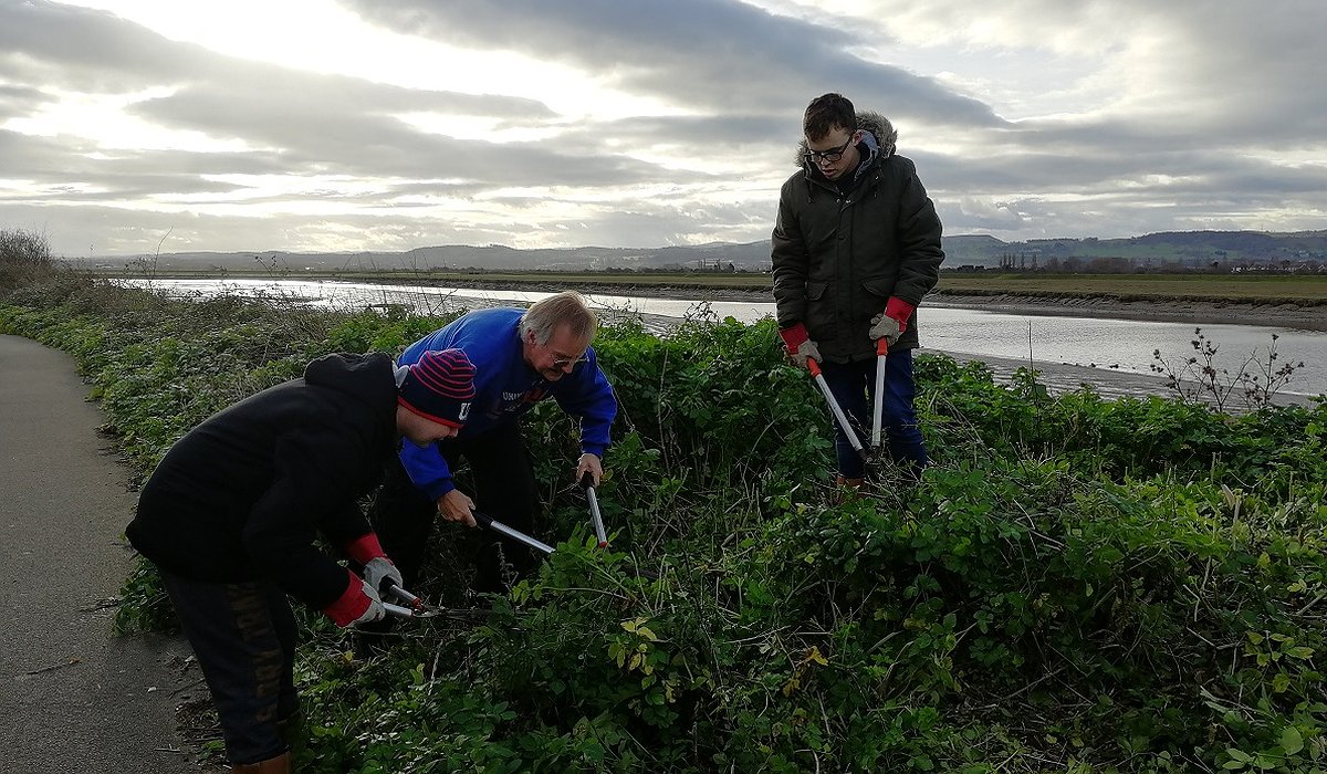 Dynion yn cymryd rhan mewn gwaith cadwraeth, yn clirio lleiniau i ffwrdd yn y Rhyl fel rhan o'r prosiect natur ar gyfer iechyd.