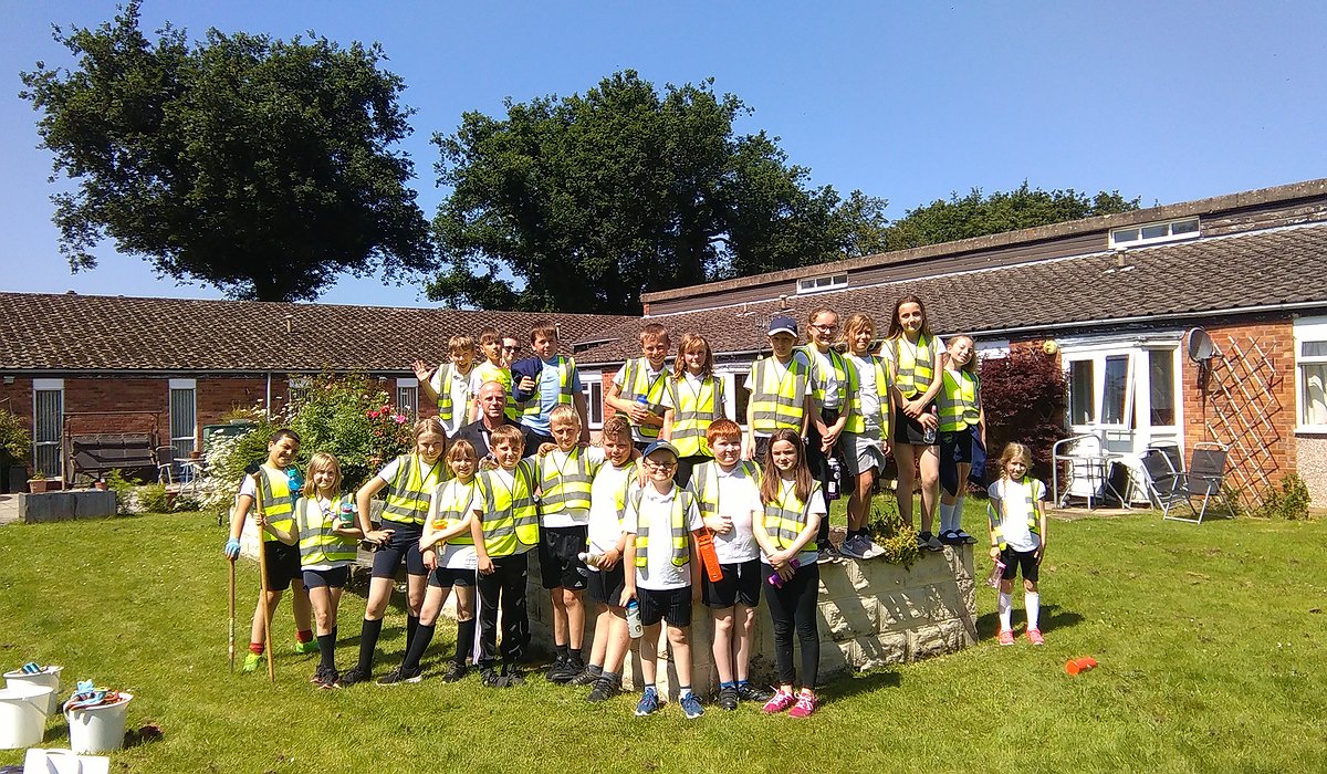 Grŵp mawr o blant ysgol ifanc yn dysgu cadw gerddi'n daclus yng Nghanolfan Gymunedol Llygadog.